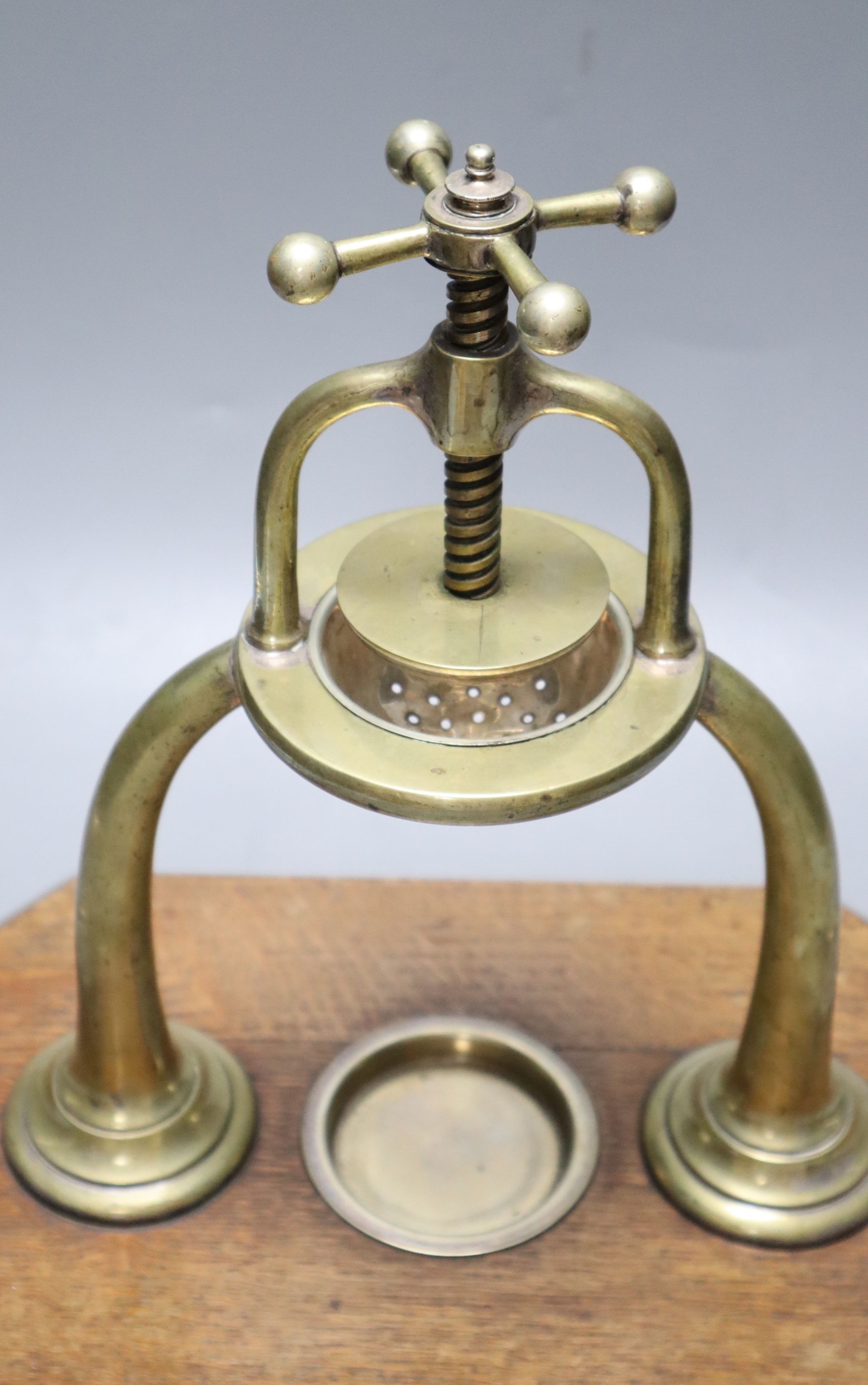 An Edwardian brass lemon squeezer on an oak plinth